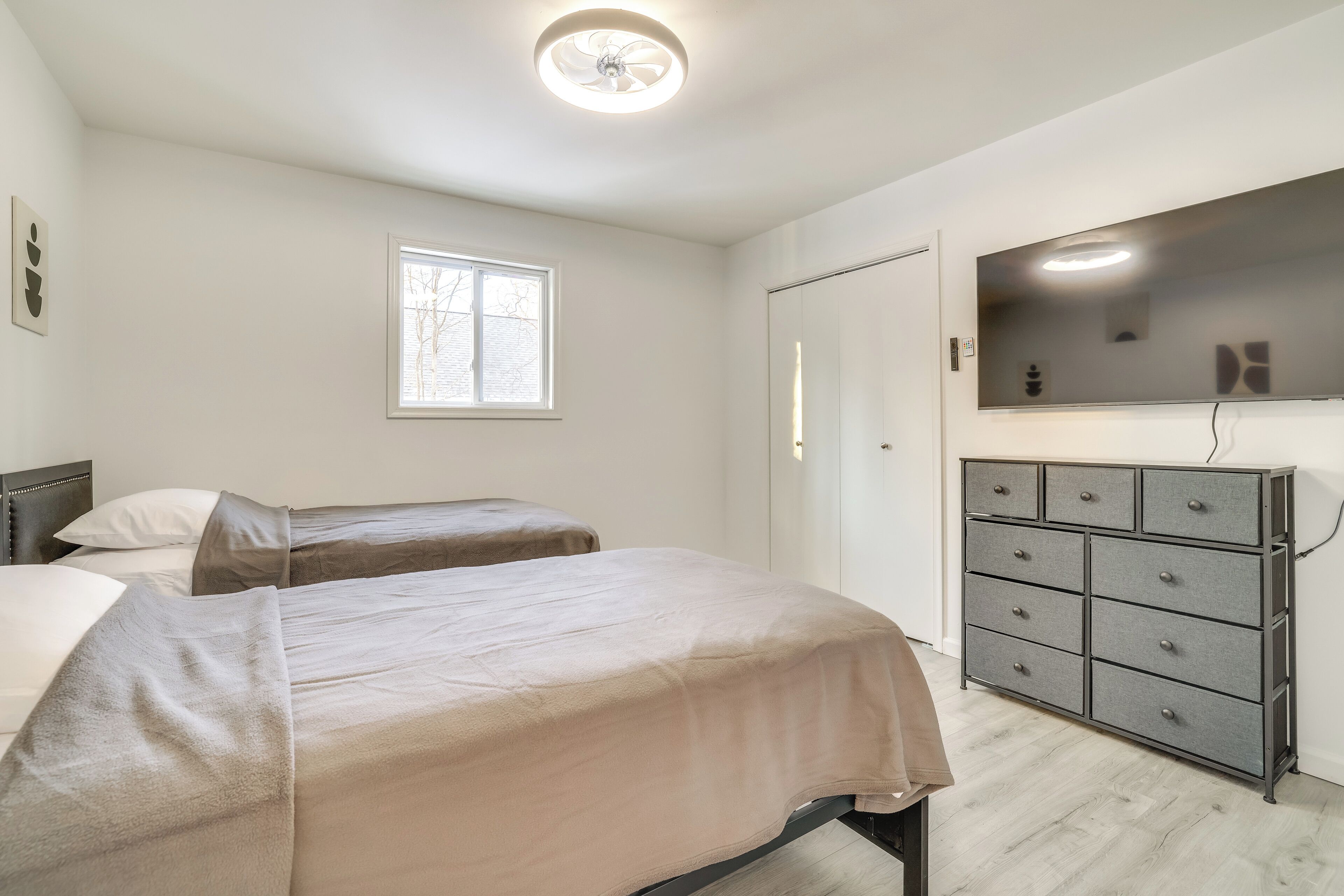 Ein Schlafzimmer mit zwei Betten, einem Schminktisch, einem Fenster und einem Deckenventilator.