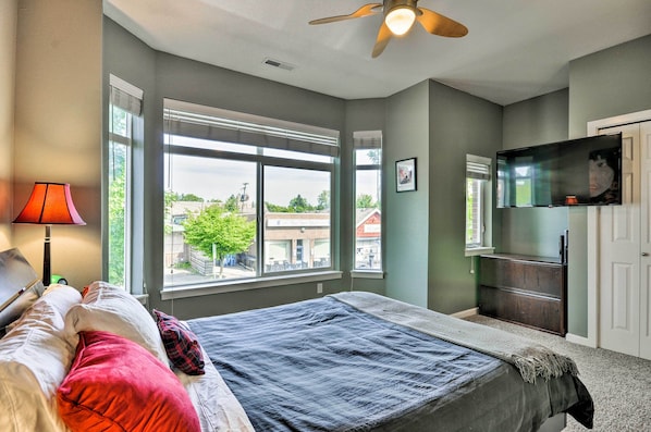 A bedroom with a bed, a desk, a lamp, a TV, and large windows. - Modern Vancouver Townhome - Right on Main St! (Vancouver)