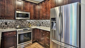 A kitchen with dark wood cabinets, stainless steel appliances, a tiled backsplash, and a granite countertop. - Modern Vancouver Townhome - Right on Main St! (Vancouver)