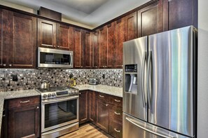 Una cocina con armarios de madera oscura, electrodomésticos de acero inoxidable, salpicadero de azulejos y encimera de granito.
