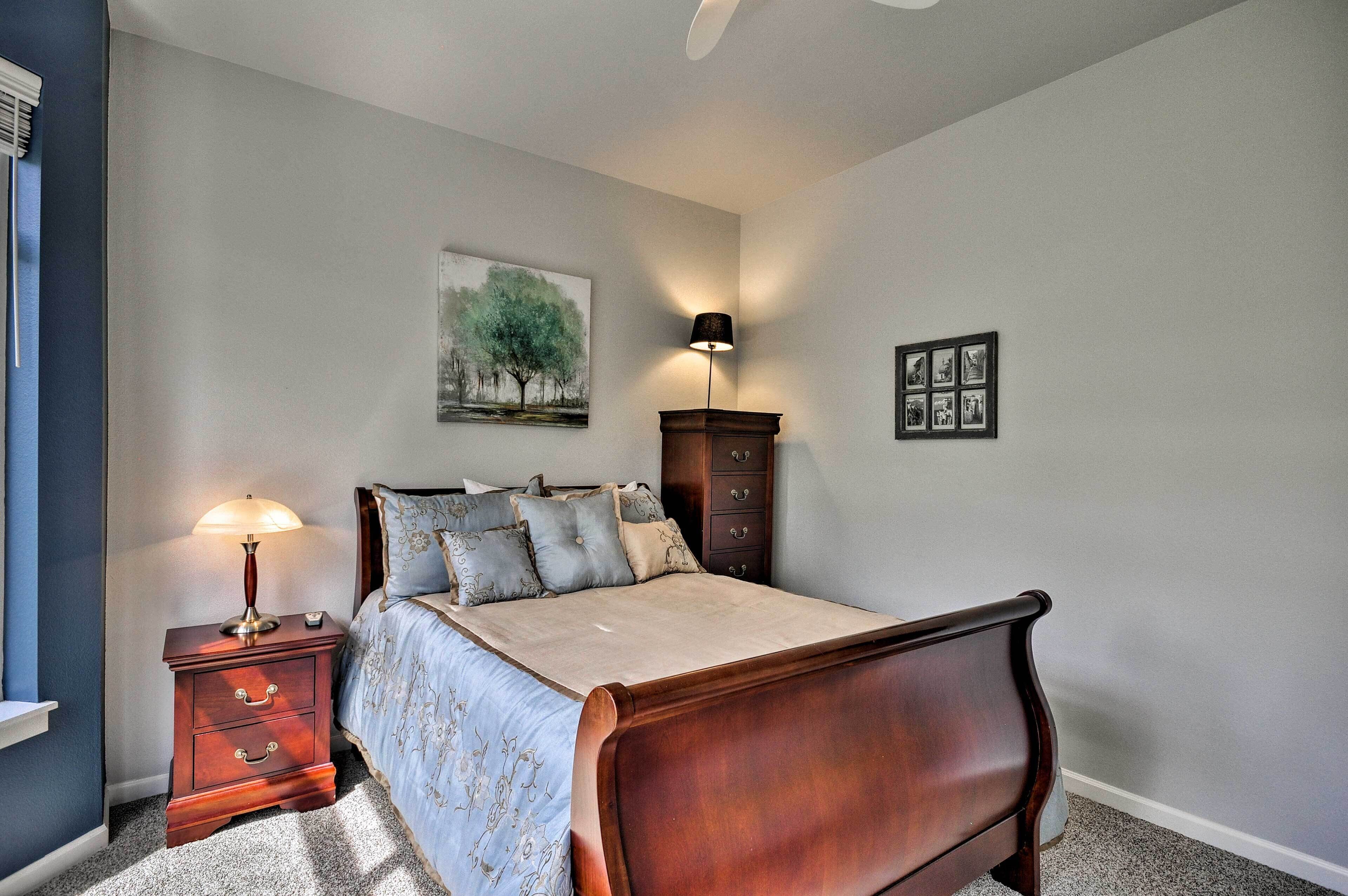 A bedroom with a bed, nightstand, lamp, dresser, and wall art.