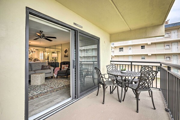 A balcony with a sliding glass door leading to a living room, furnished with a sofa, chairs, and a table.