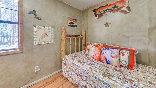 A bedroom with a wooden bunk bed, a patterned bedspread, and wall decorations including a painted sunset, a horse silhouette, and a star. - Deck & Hot Tub Bear Country Cabin, Upper Canyon (Ruidoso)