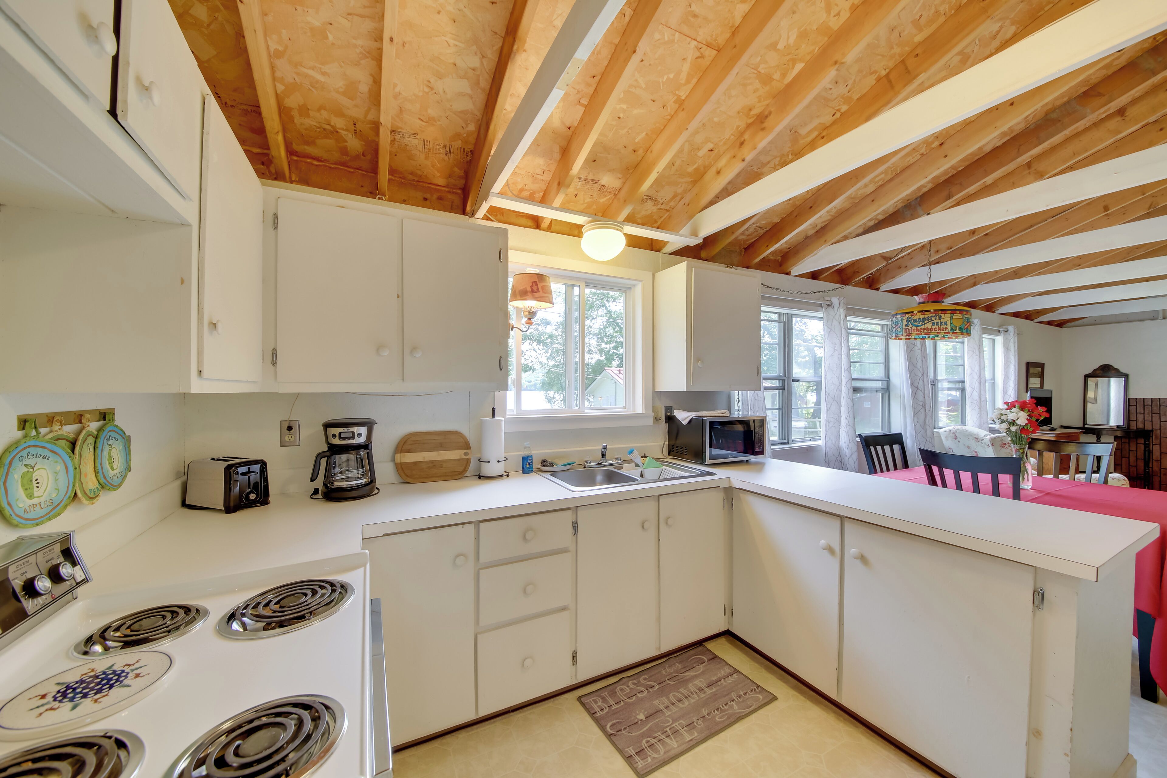 A kitchen with white cabinets, a stove, a sink, and a dining area with a red tablecloth.