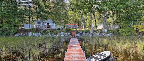 A wooden dock leading to a house surrounded by trees and a pond.