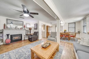 Una sala de estar con chimenea, ventilador de techo, comedor con mesa y sillas, y sofá.