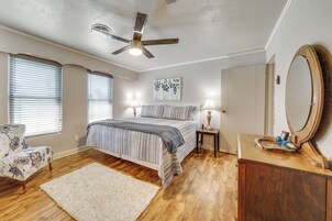 Un dormitorio con una cama, una silla, una mesita de noche, un espejo y un ventilador de techo.