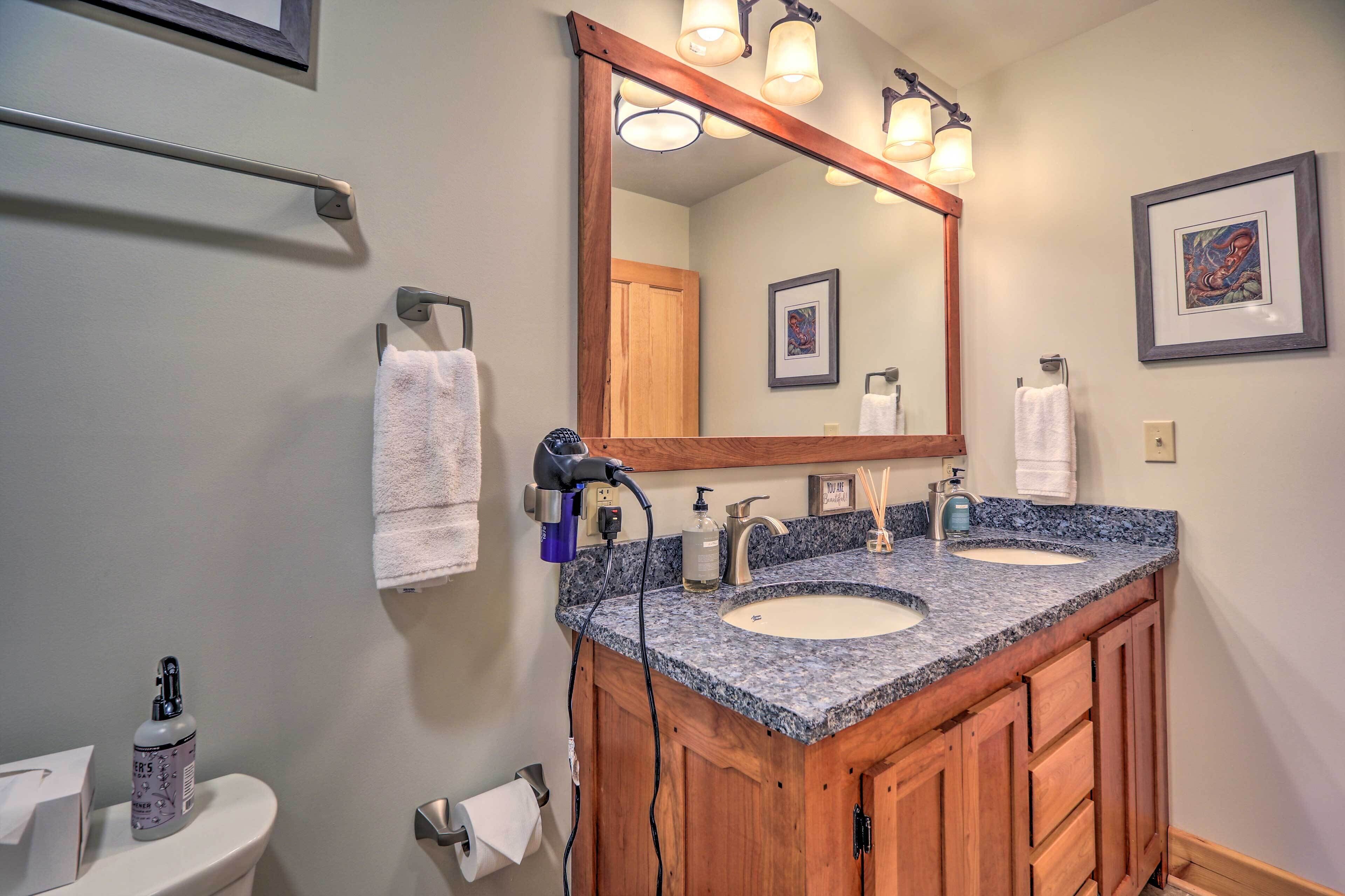 A bathroom with a double sink, wooden vanity, a large mirror with lights, and a towel rack.