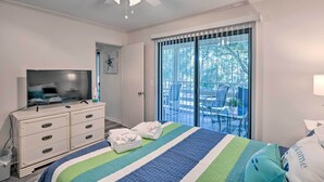 Un dormitorio con cama, cómoda, televisor y puerta corrediza de vidrio a un balcón.