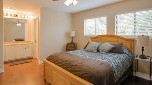 A bedroom with a wooden bed, a ceiling fan, a vanity with lights, and two windows with blinds. - Baton Rouge Townhome w/ Pool Access - 7 Mi to Lsu! (Baton Rouge)
