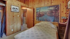 Ein Holzhüttenraum mit einem Bett, einem Schminktisch und einem Gemälde eines Sees.