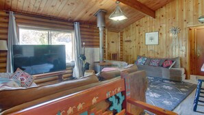 L’intérieur chaleureux d’un chalet en rondins, avec un banc en bois, un canapé, un téléviseur et un moulin à vent décoratif.