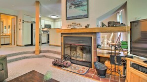 Un salón amplio con chimenea, televisor y cocina al fondo.