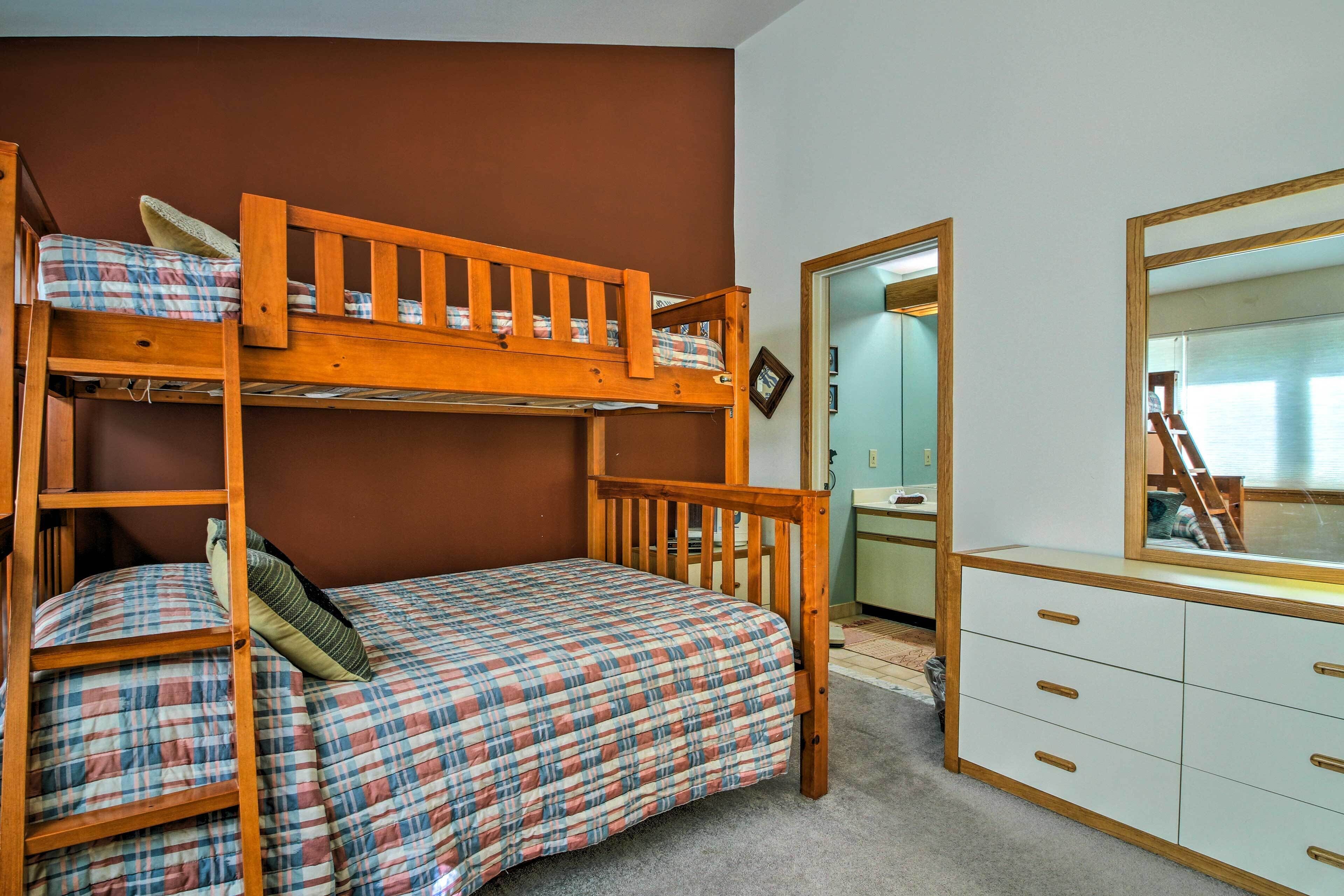 A bunk bed with a plaid bedspread, a wooden dresser with drawers, and a mirror above the dresser.