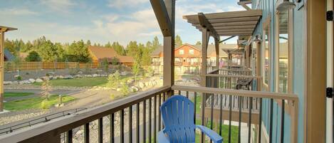 A balcony with a blue chair, wooden railings, and a view of a residential area with houses and trees.