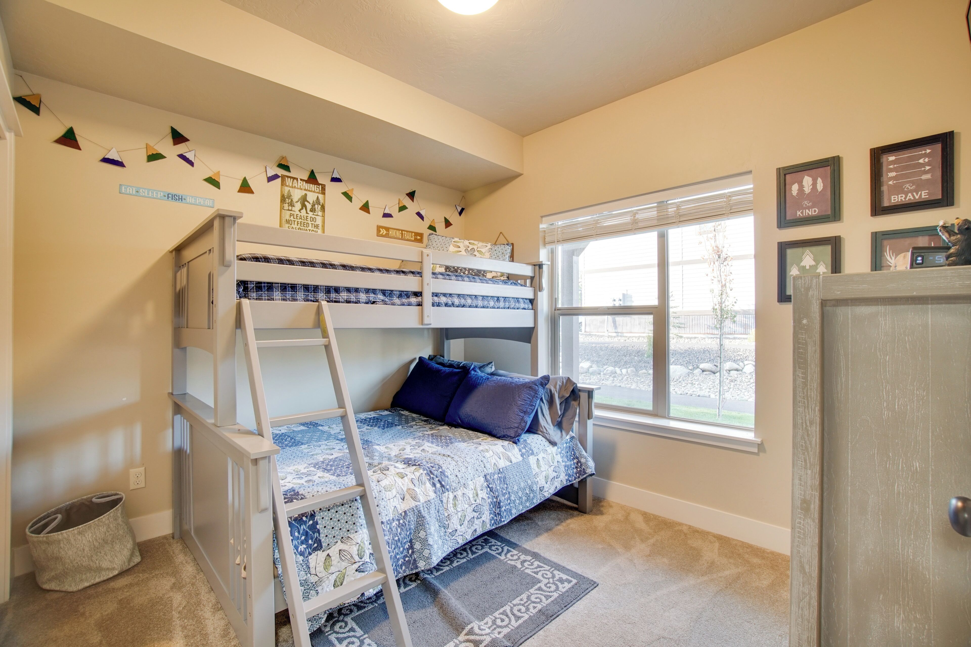 A child's bunk bed with a ladder, a window with blinds, and a rug on the floor.