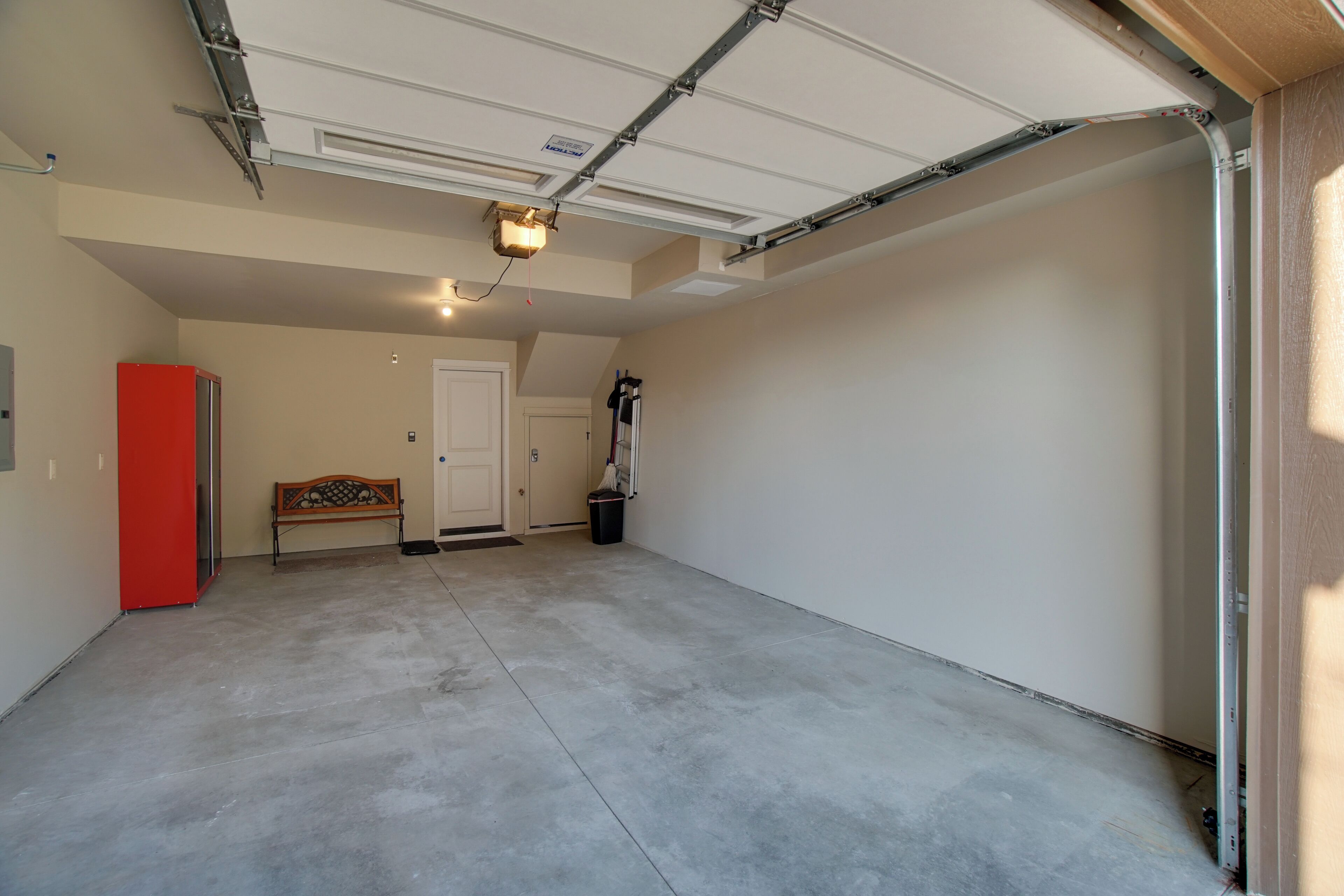 A garage with a concrete floor, a red refrigerator, a bench, and a door.