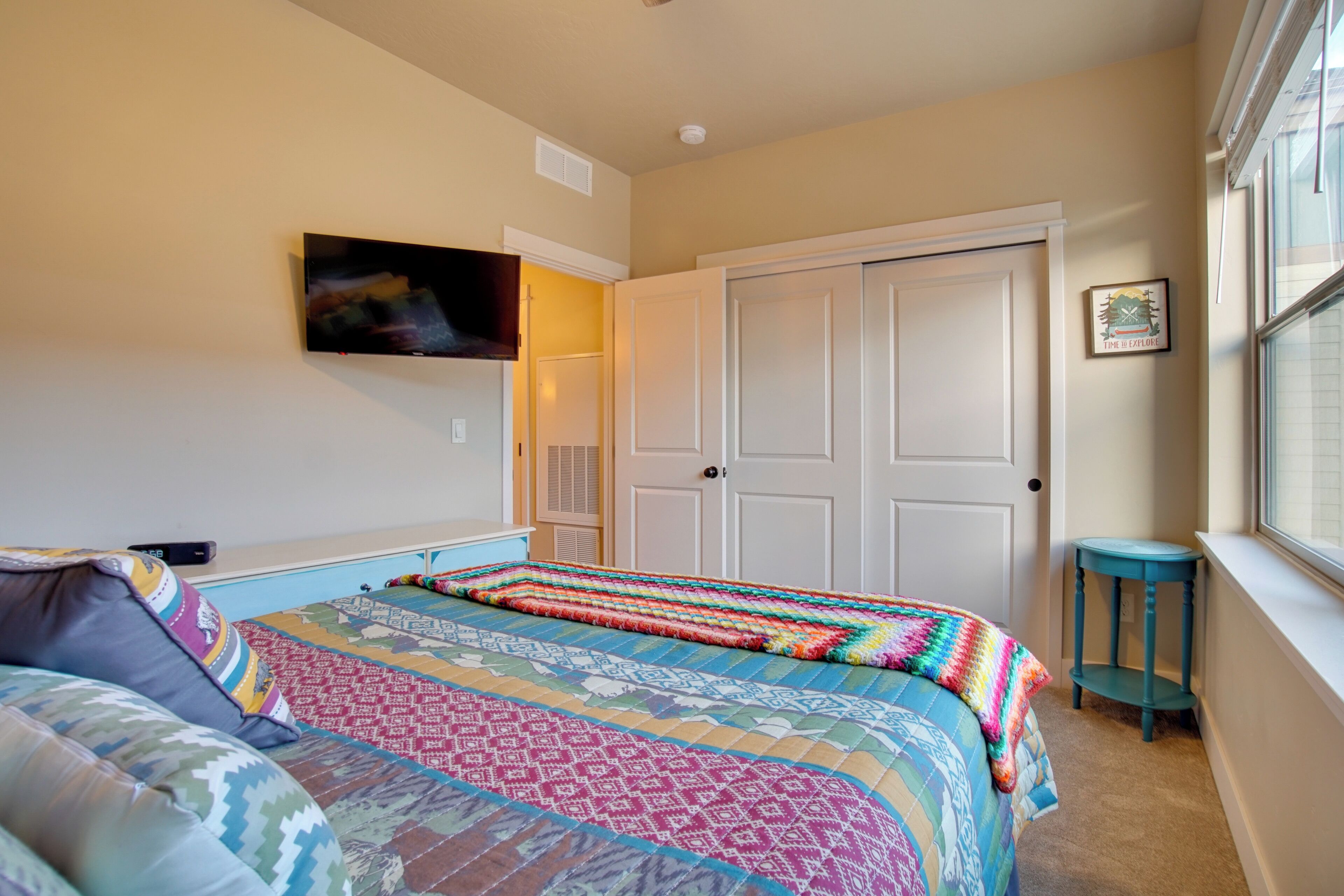 A bedroom with a bed, a TV mounted on the wall, a door, and a window.