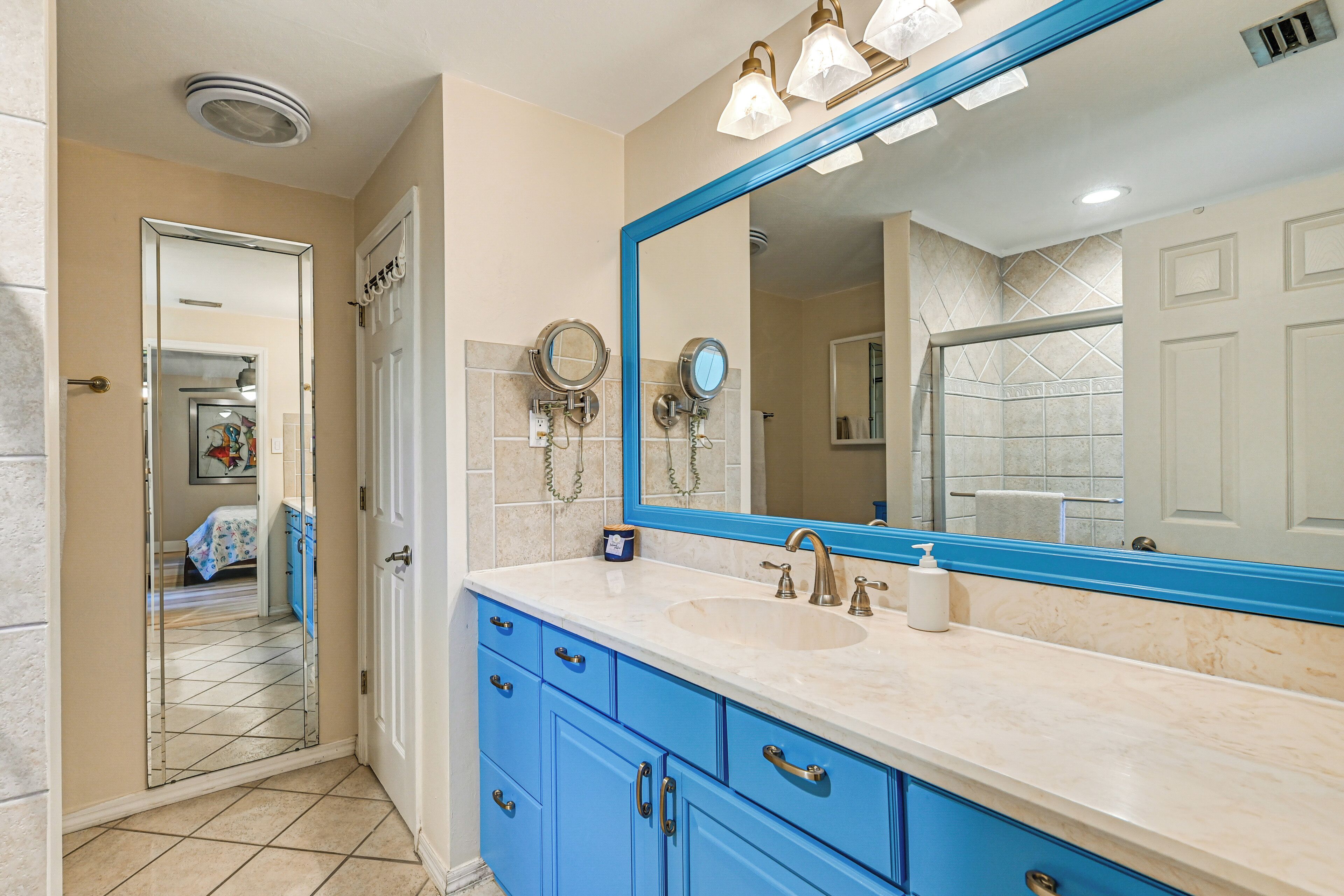 Une salle de bain avec un grand miroir, des meubles bleus et un lavabo.