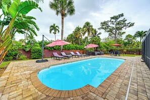 A swimming pool with lounge chairs and umbrellas, surrounded by palm trees and greenery. - 4 Mi to Beach: Pet-friendly Home in Naples! (Naples)