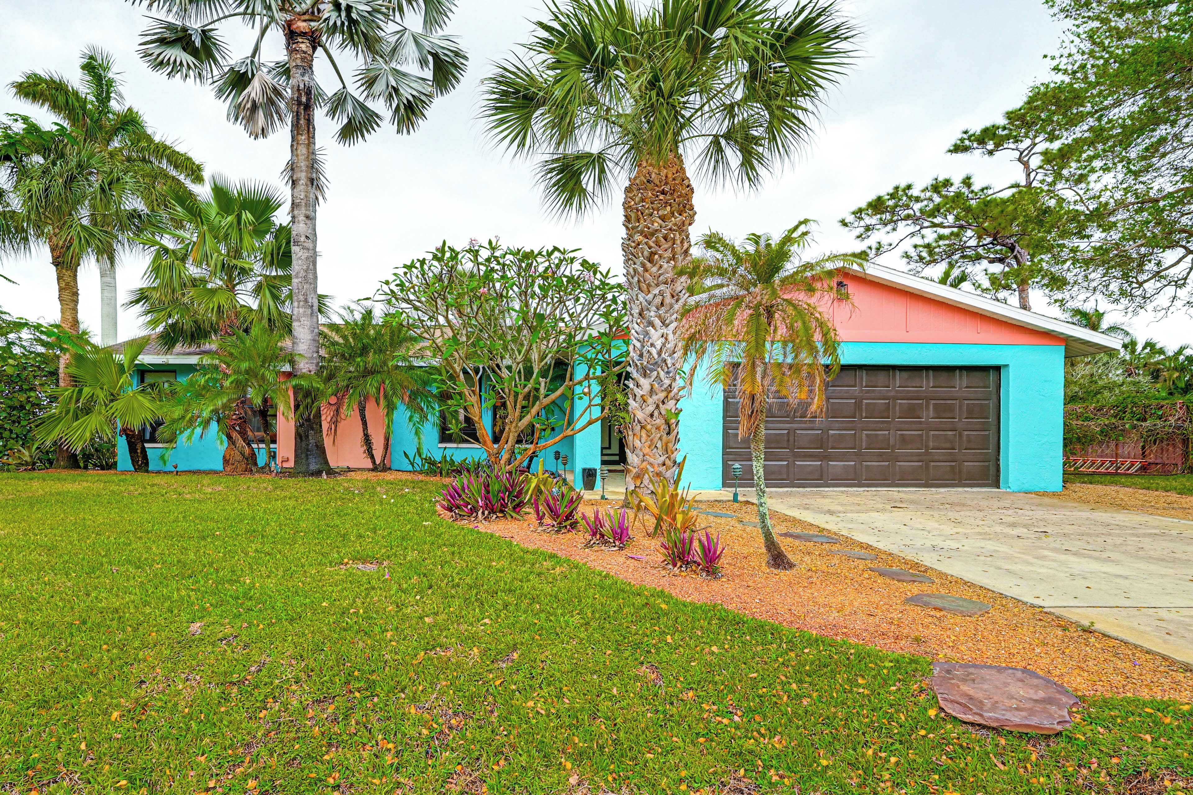 A modern house with a blue and orange exterior, surrounded by a well-maintained lawn and palm trees.