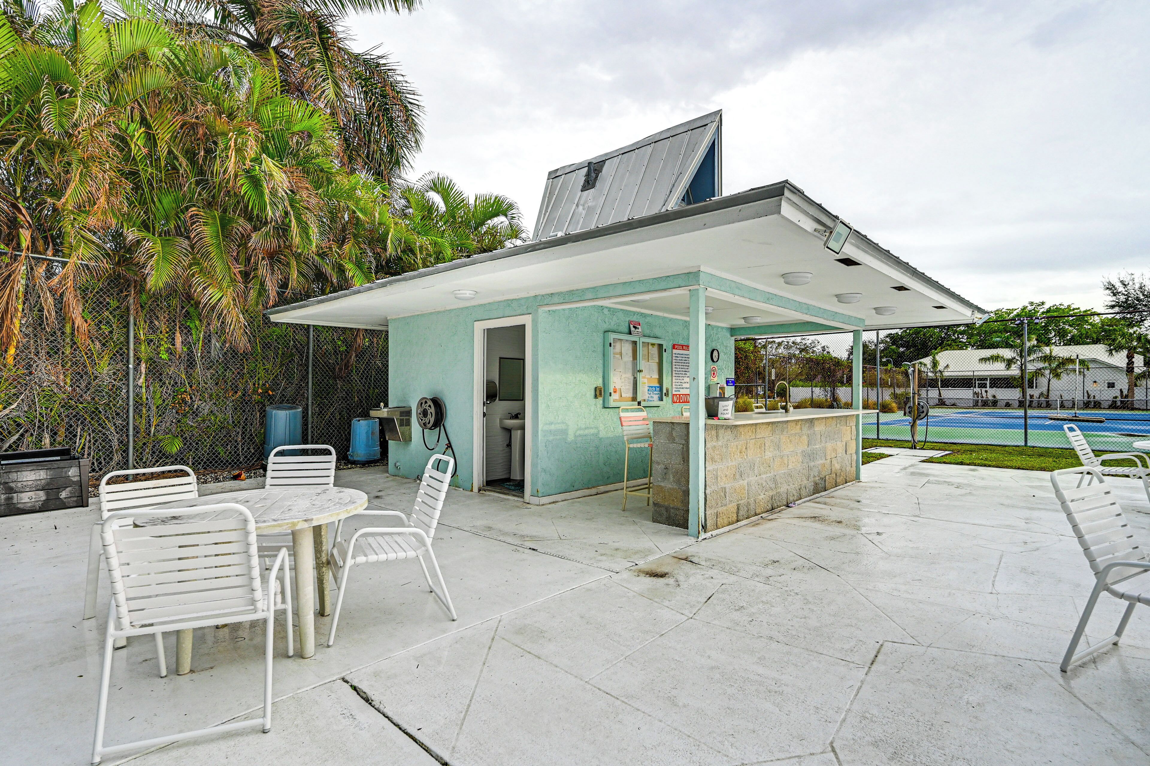 A small outdoor bar area with a glass enclosure, white metal chairs, and a table.