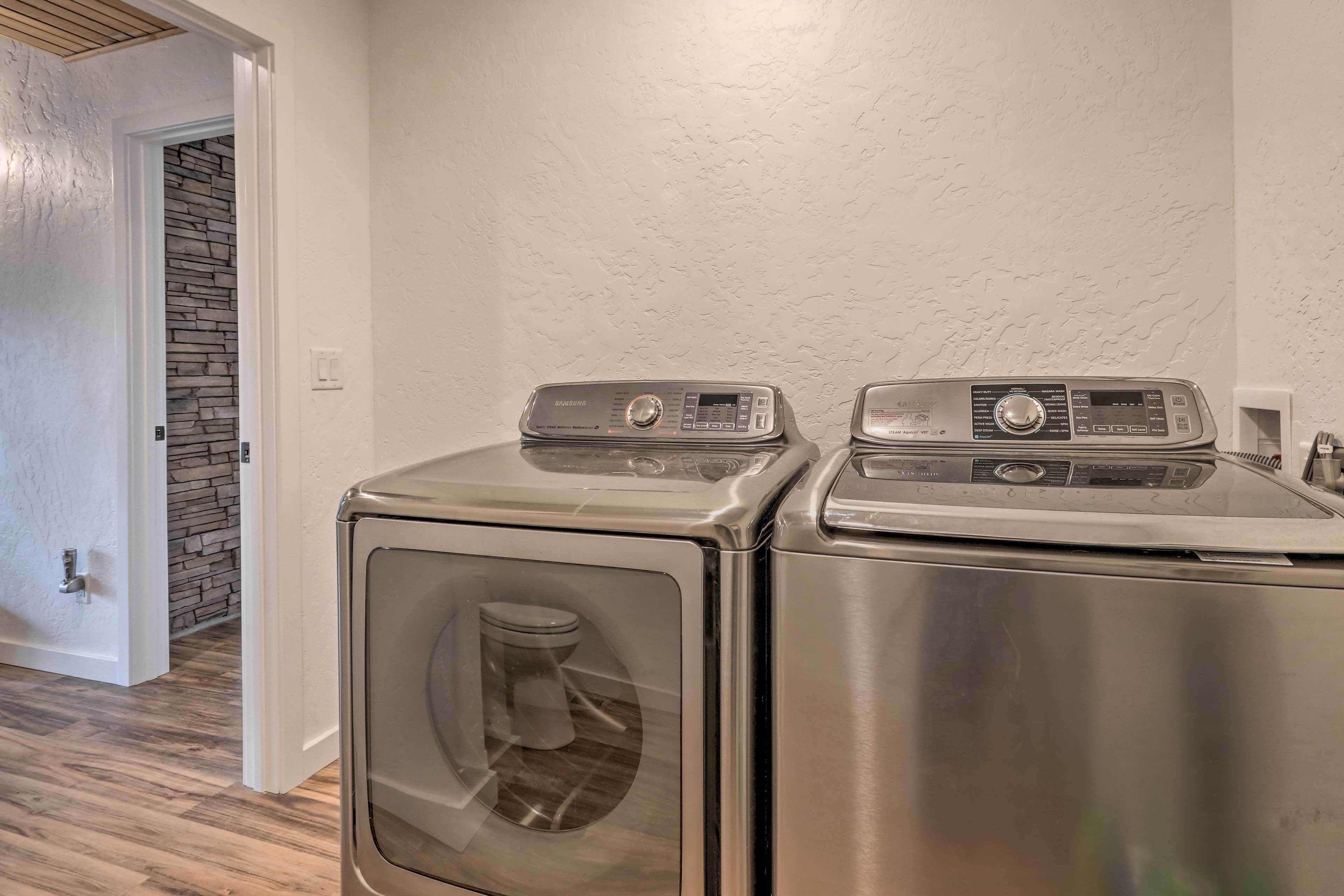 Une buanderie équipée de deux lave-linge et deux sèche-linge à chargement frontal en acier inoxydable, d’un mur décoratif en pierre et d’un plancher en bois.