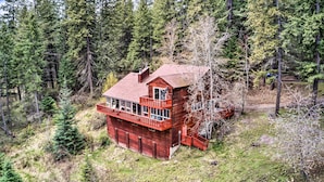 Une cabane en bois à deux étages, dotée d’un balcon et entourée d’une zone boisée.