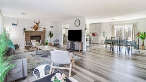 A spacious living room with a fireplace, a television, and a dining area with a table and chairs. - Hot Tub, Game Room: Peaceful Poconos Home! (Long Pond)