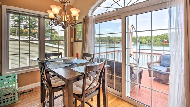 A dining area with a table and chairs, large windows, and a view of a lake. - Waterside Haven on Milton Pond w/ Deck & Boat Dock (Milton)