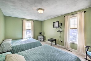 A room with two beds, a television, a fan, and a window with curtains.