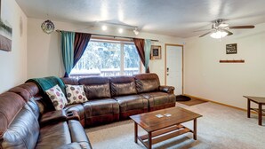 A living room with a leather sofa, a wooden coffee table, a ceiling fan, and a window with curtains. - Peaceful Nature Escape w/ Deck in North Pole! (North Pole)