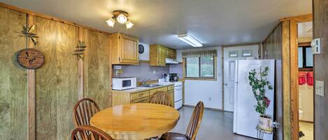 A compact kitchen with wooden cabinets, a dining table with chairs, a refrigerator, and a microwave.