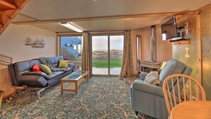 Una sala de estar acogedora con sofá, sillón y mesa de centro, un televisor montado en la pared y un ventanal con vistas al exterior.