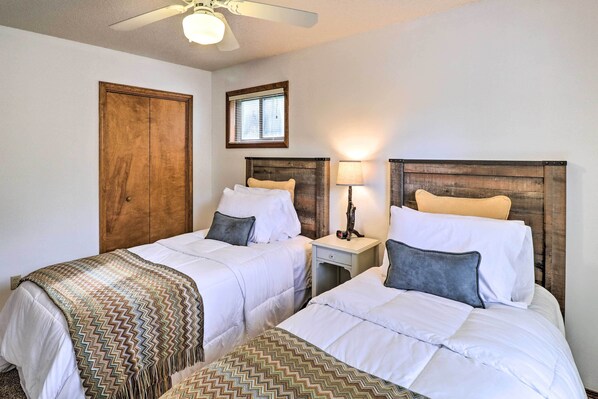 A hotel room with two beds, wooden headboards, a nightstand with a lamp, a ceiling fan, and a window with blinds. - Private Riverfront Home on the White River! (Norfork)