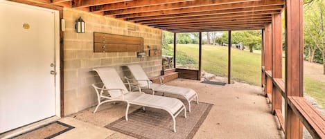 Een overdekt terras met twee loungestoelen, een stenen muur en een deur.