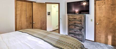A bedroom with a bed, wooden wardrobe, and a TV mounted on the wall.