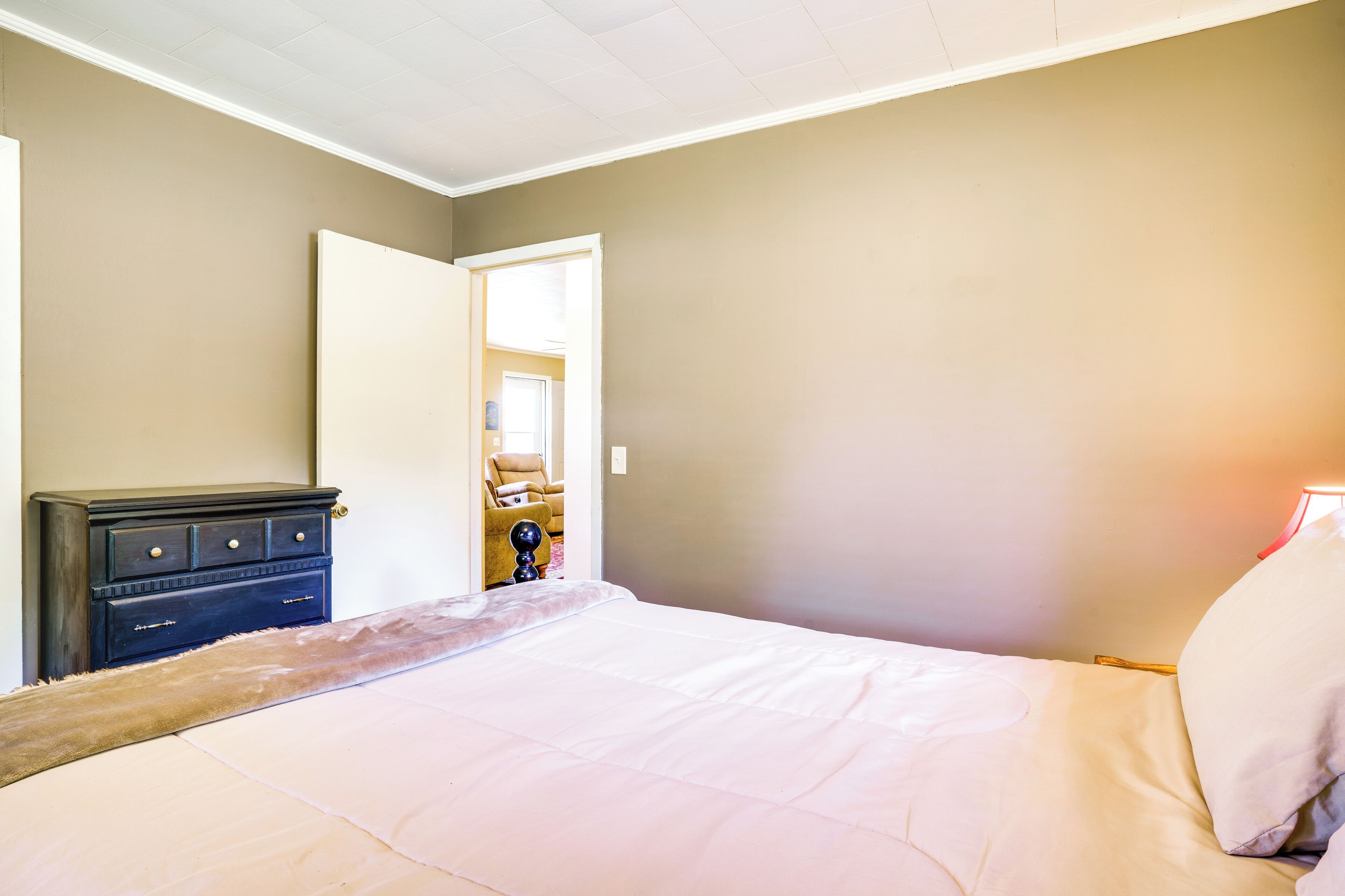 A bedroom with a bed, a dresser, and a door leading to another room.
