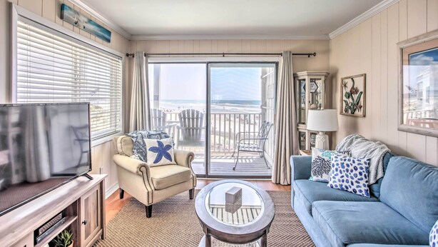 A living room with a TV, beige sofa, blue sofa, and a balcony with a view of the beach. - North Myrtle Beach Condo w/ Stunning Ocean Views! (North Myrtle Beach)