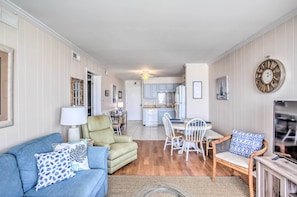 A living room with a sofa, armchair, and dining table. There is a kitchen in the background with cabinets and a refrigerator. - North Myrtle Beach Condo w/ Stunning Ocean Views! (North Myrtle Beach)