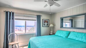 A bedroom with a bed, a chair, a window with curtains, a ceiling fan, a lamp, and a framed picture on the wall. - North Myrtle Beach Condo w/ Stunning Ocean Views! (North Myrtle Beach)