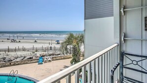 A balcony with a view of a beach, a pool, and a building with a white exterior. - North Myrtle Beach Condo w/ Stunning Ocean Views! (North Myrtle Beach)