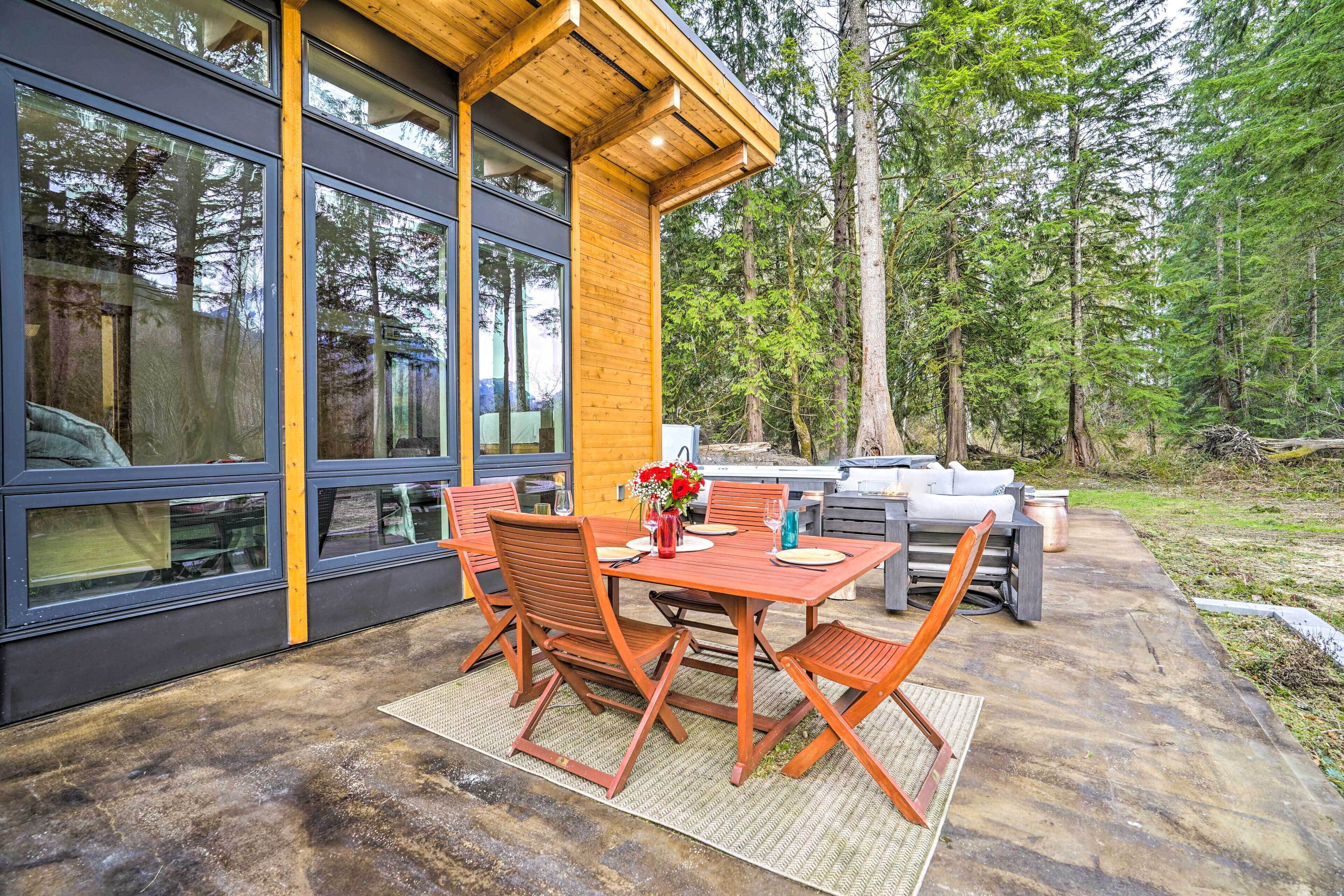 A modern outdoor dining area with a wooden table and chairs, a vase with flowers, and a grill.