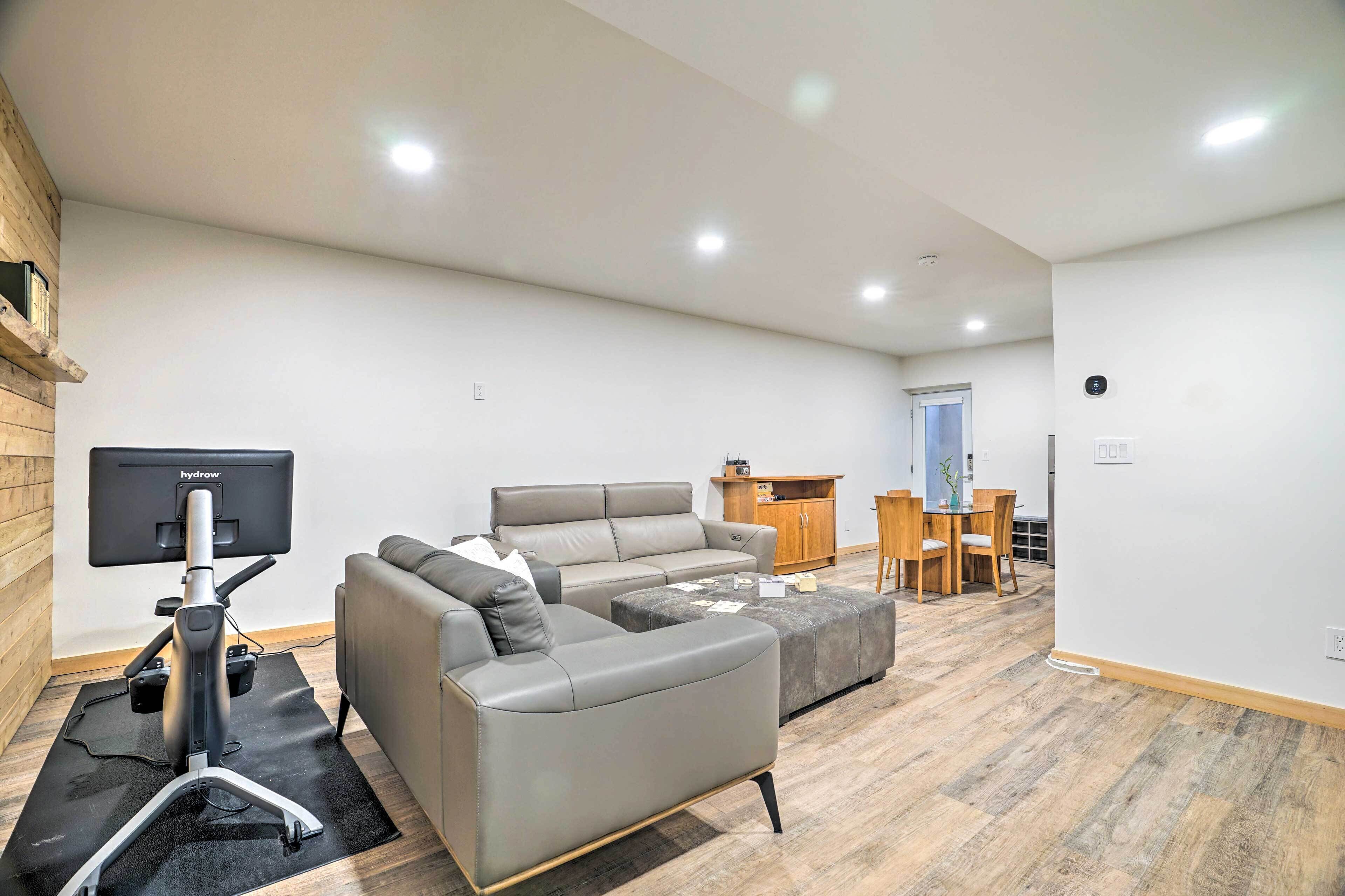 A modern living room with a grey sofa, ottoman, and a flat-screen TV on a stand.