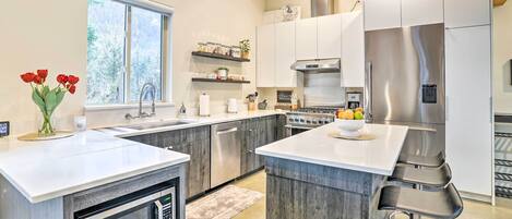 Una cocina moderna con una isla central, electrodomésticos de acero inoxidable y vigas de madera en el techo.