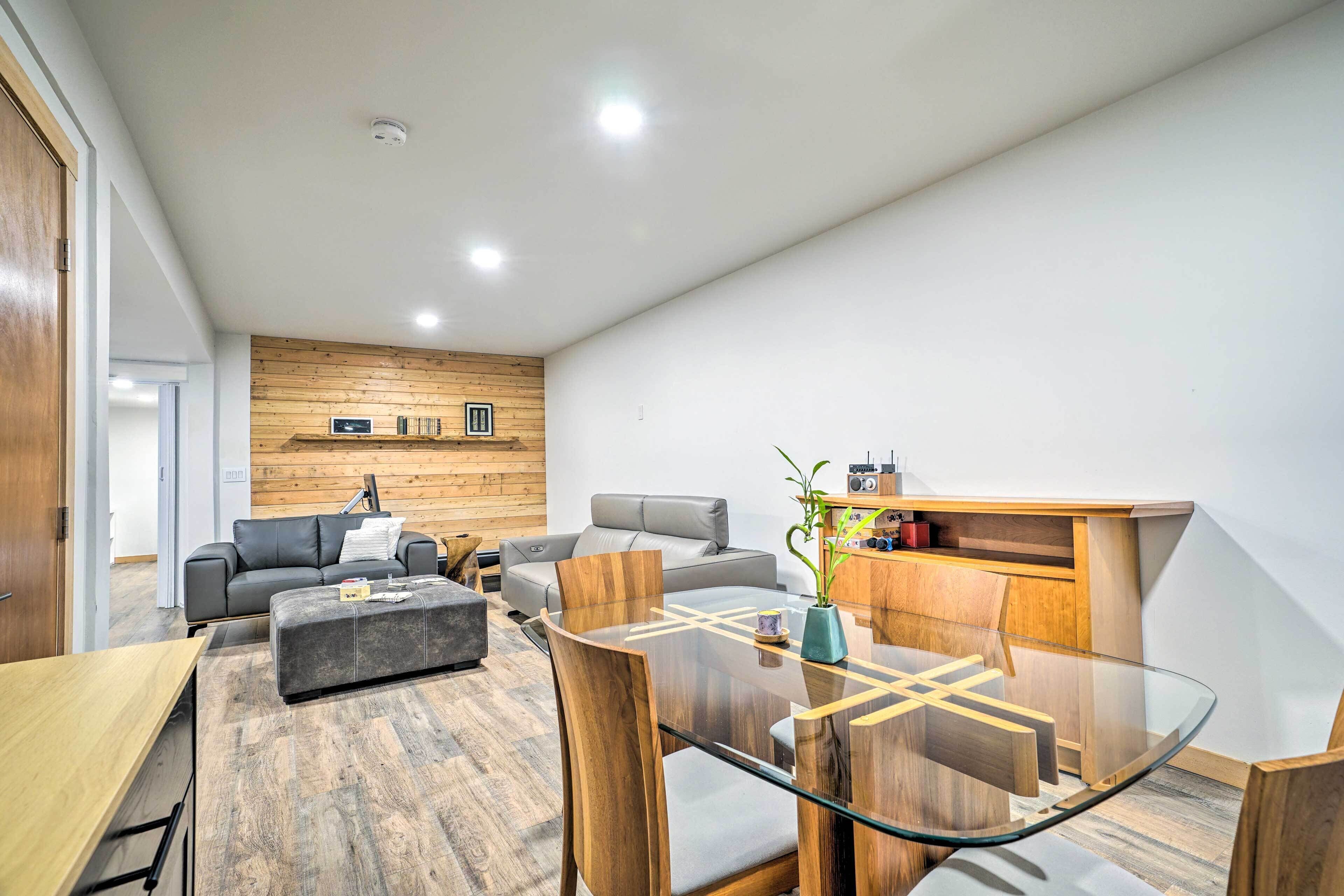 Un salon moderne avec une table à manger à plateau de verre, des canapés en cuir et un mur décoratif en bois.