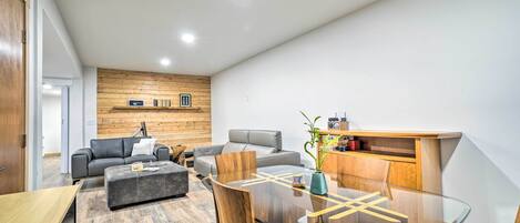 Un salon moderne avec une table à manger à plateau de verre, des canapés en cuir et un mur décoratif en bois.