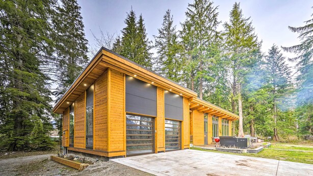 Eine moderne Holzhütte mit großen Garagentoren, umgeben von dichtem Wald.