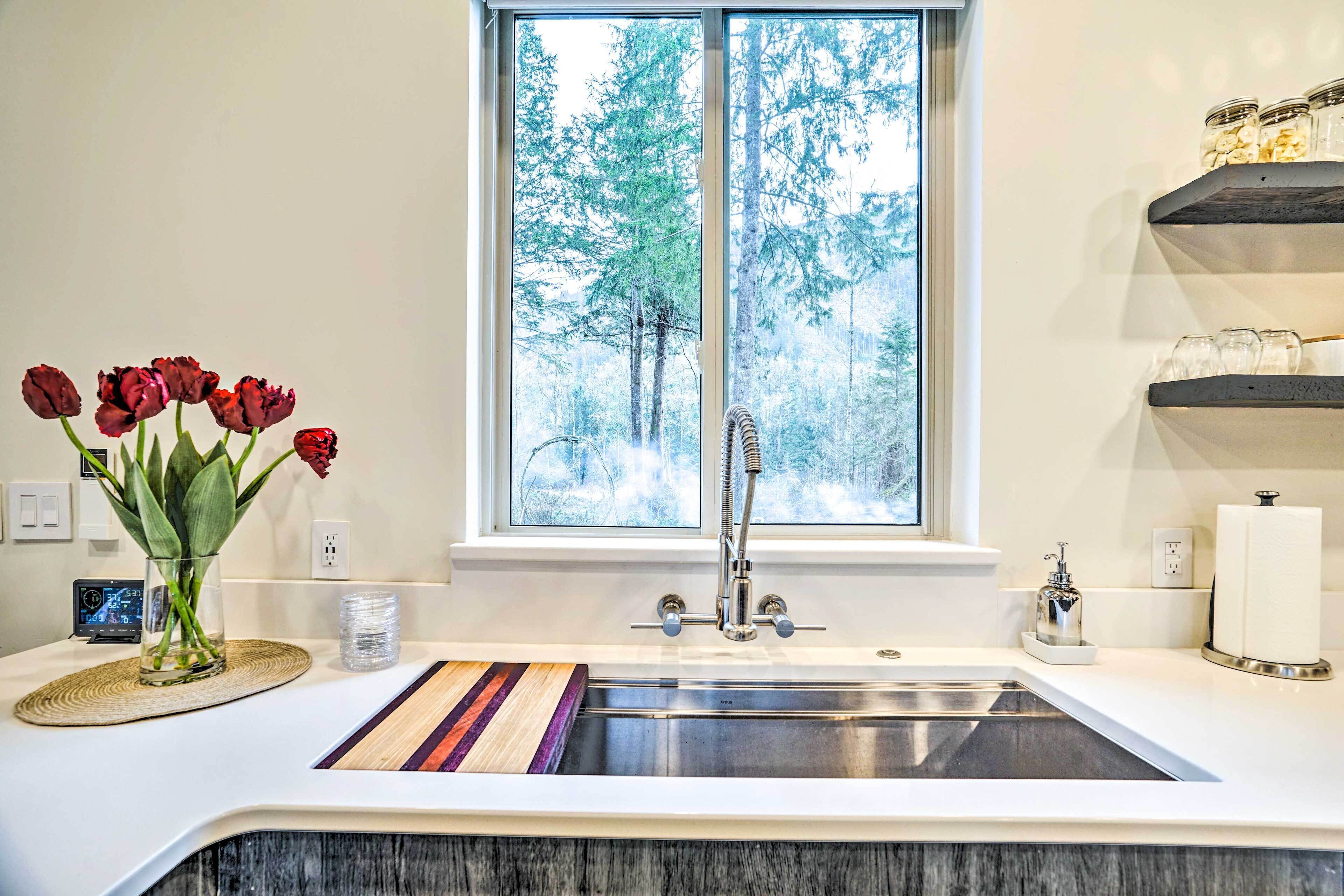 A modern kitchen with a large window, a stainless steel sink, and a vase of red tulips on the counter.