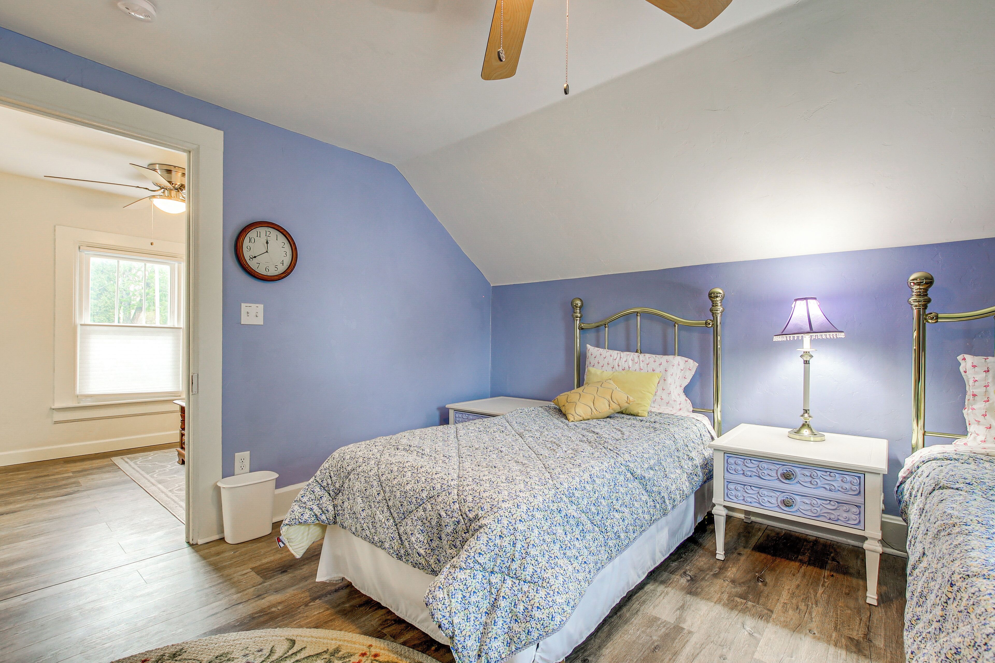 A bedroom with a sloped ceiling, a bed with a floral bedspread, a nightstand with a lamp, and a wall clock.